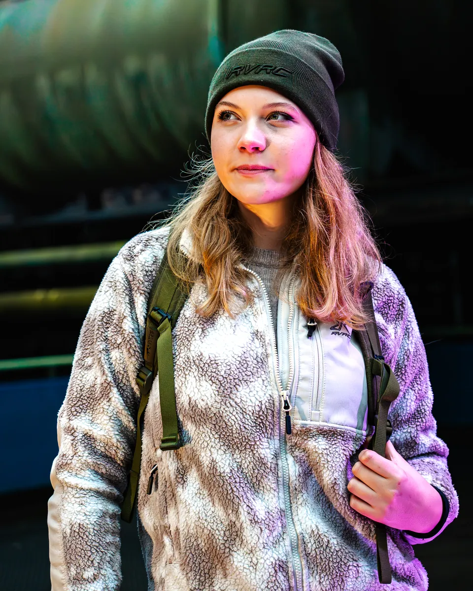 Outdoor-Porträt mit Mütze und Rucksack vor Industriekulisse