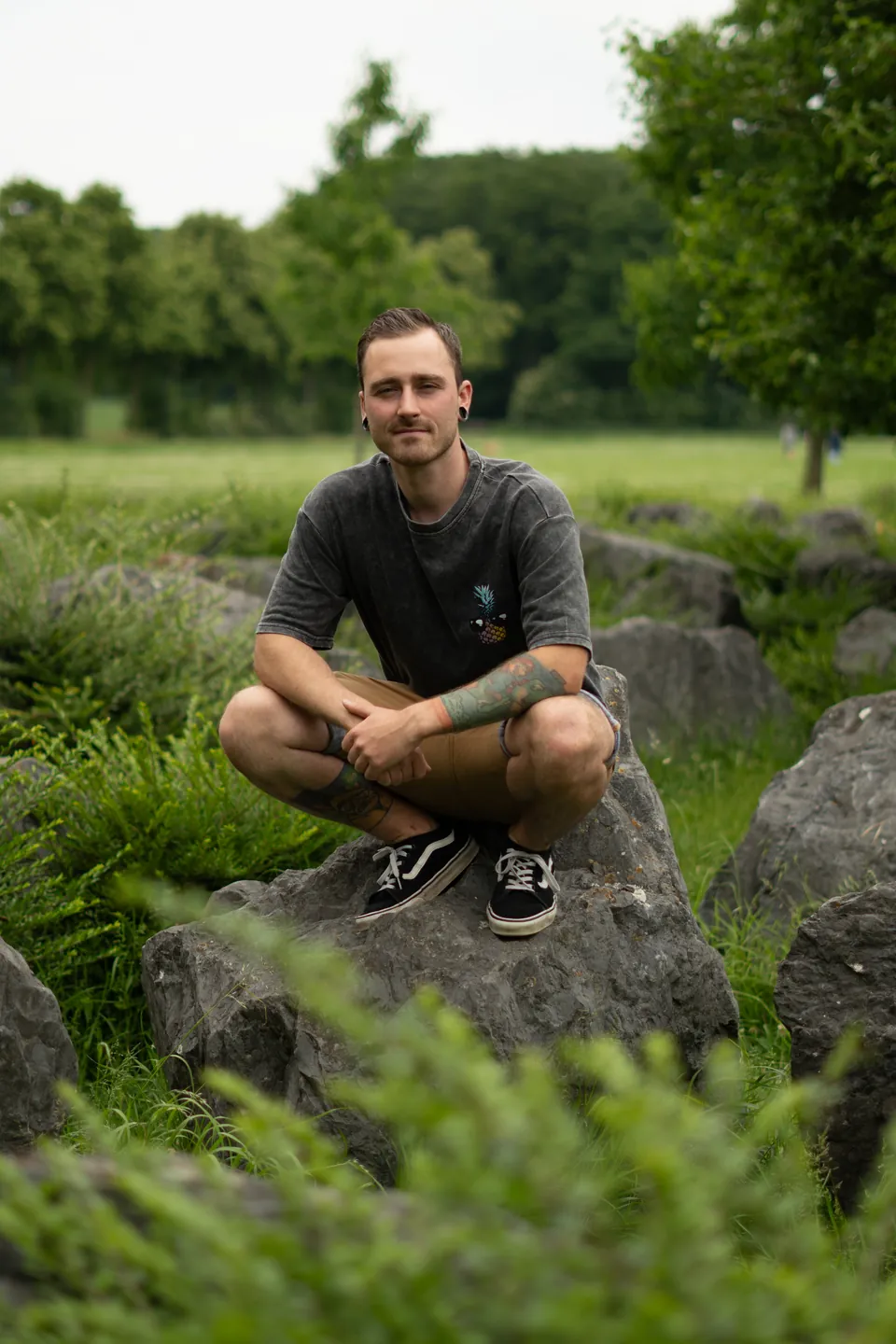 Justin Pohl sitzt lächelnd auf einem Felsen im Grünen